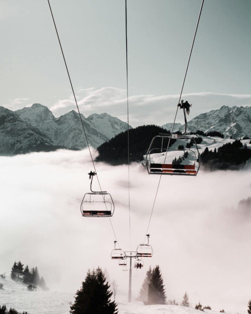 A chairlift glides through a misty mountain landscape, revealing snowy peaks and expansive winter scenes.